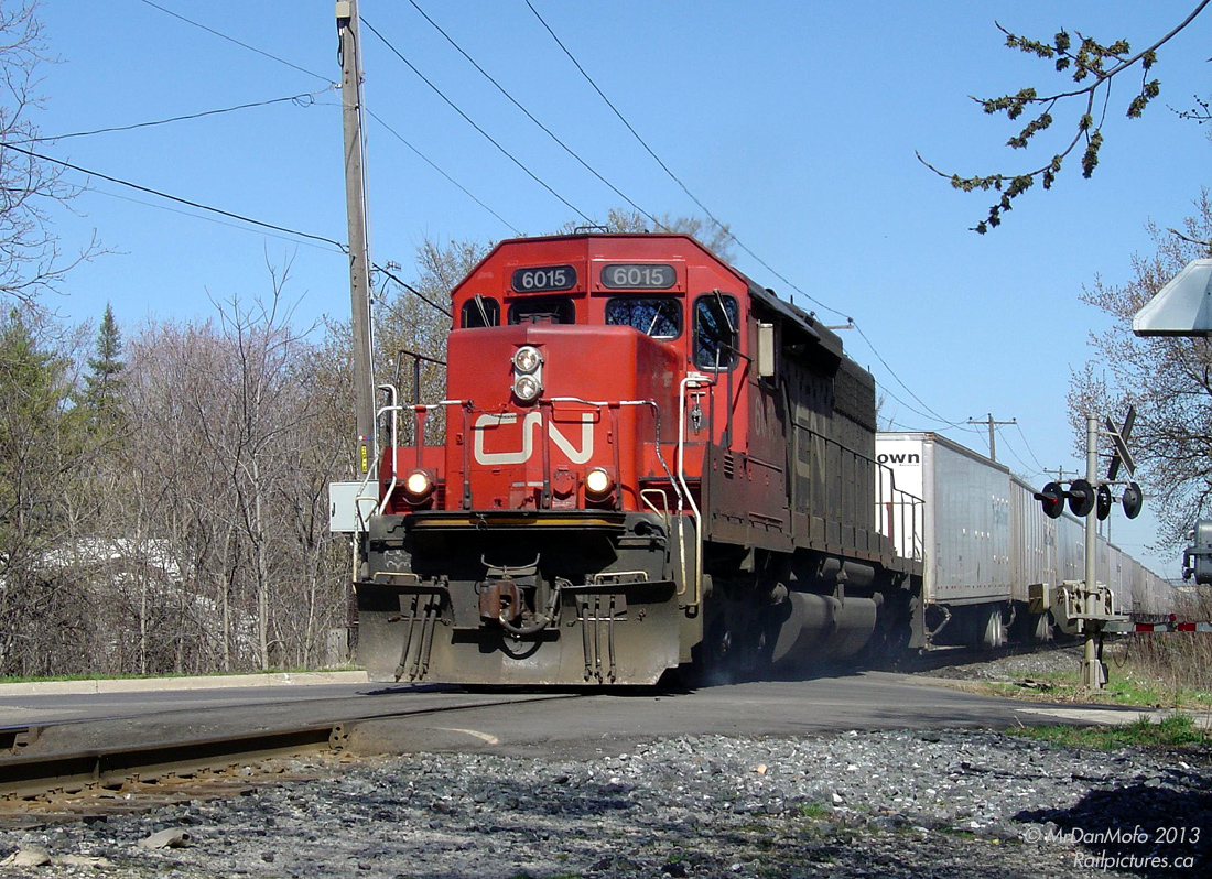 Beat the Rush.  CN train 145 "The Roadrailer" beats the evening GO train rush as it rolls through the single track territory of the busy CN Halton Subdivision, minutes before the first scheduled GO train is due in downtown Brampton. Once the GO rush hits full swing, the Rail Traffic Controller must juggle a steady flood of half hourly westbound GO and VIA trains coming from the south track at Bramalea, through the single track between Peel to Brampton East, on to the north for Brampton Station, through the single-tracked Credit River bridge and into the GO commuter compound at Georgetown. All the while trying to manage various eastbound and westbound CN through-freights on the same tracks, the occasional local out switching, and that kooky GEXR 431/432.  The Triple Crown Roadrailer, made up of somewhat boring truck trailers designed to ride on rail bogies, has always warranted precisely one unit. This one unit is often a wildcard from day to day, ranging from a clapped-out rusty GP40-2W, a well-worn secondhand or rebuild SD40, a ho-hum GE -9W, to a brand new SD70M-2. Today it's one of CN's 29 rebuilt SD40u units (or SD40-2Q, or SD40-3, or GF-630a, whatever!) kicking up crossing dust over James St. The lucky Batman sign scribbled on its front pilot must be giving it an extra bit of good luck today.  Hard on his heels is GO #281 "The Bramalea Flip" - the afternoon 7-car GO train that ping-pongs between Bramalea and Toronto Union, which makes its final trip all the way to downtown Brampton to kick off the flood of evening GO trains. In only 3 minutes, the green and white train will zip into view and begin slowing for the station.  Today, the SD40u's have been rebuilt for yard service, half of the James-John St. crossing has been closed, the single-track juggling has been eliminated with double-tracking and platforms on both sides of the tracks, and the afternoon GO train has been temporarily cancelled. But at least the Roadrailer still runs.