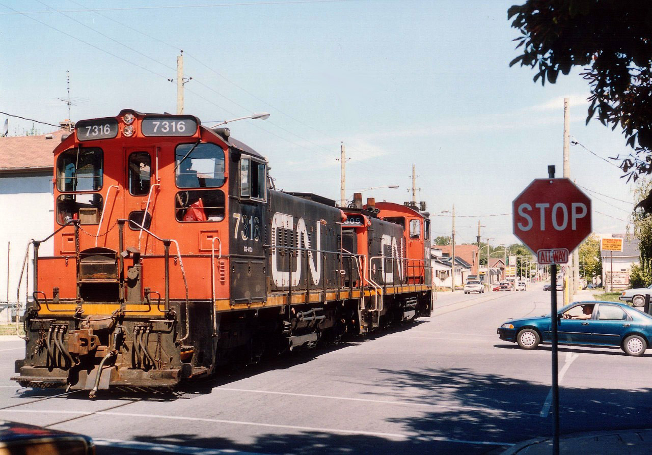 CN would relinquish control of this old branchline in downtown Thorold in just over a month to the fledgling Port Colborne Harbour Railway (Trillium; as all the non-core trackage in Niagara west of the canal was sold off by CN on September 19, 1999. The old Pine St. trackage was once part of the Fonthill Spur, most of which was ripped up many years ago. On this day CN 1316 and 1305 are on their way north to track's end to fetch boxcars at an industry there. I believe this image taken at the corner of Pine St. S and Sullivan Av. That lone rail customer along this section of track has closed and Pine St street running is no more.  The locos: 7316 went to Lambton Diesel Specialists in 2012 after being retired by CN in 2003. CN 7305 is now Prince Rupert Grain 7305.