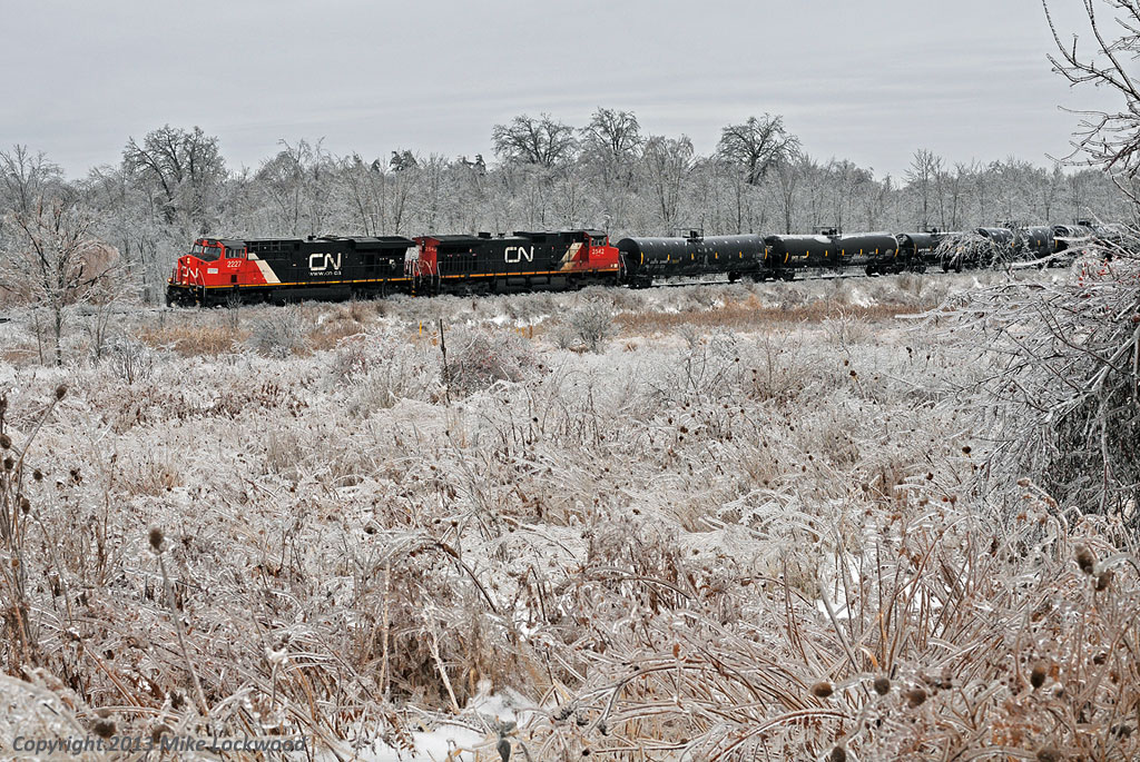 'Ice to see you' - McBain. Dropping down the grade to Liverpool Jct., CN 2227 and 2542 ease 376's train at a greatly reduced speed towards the Ressor Road grade crossing. With the obvious extent of the ice storm that had just passed, and the havoc it reeks on electrical infrastructure, CN can't take for granted that the grade crossing signals are working properly through here. 1119hrs.