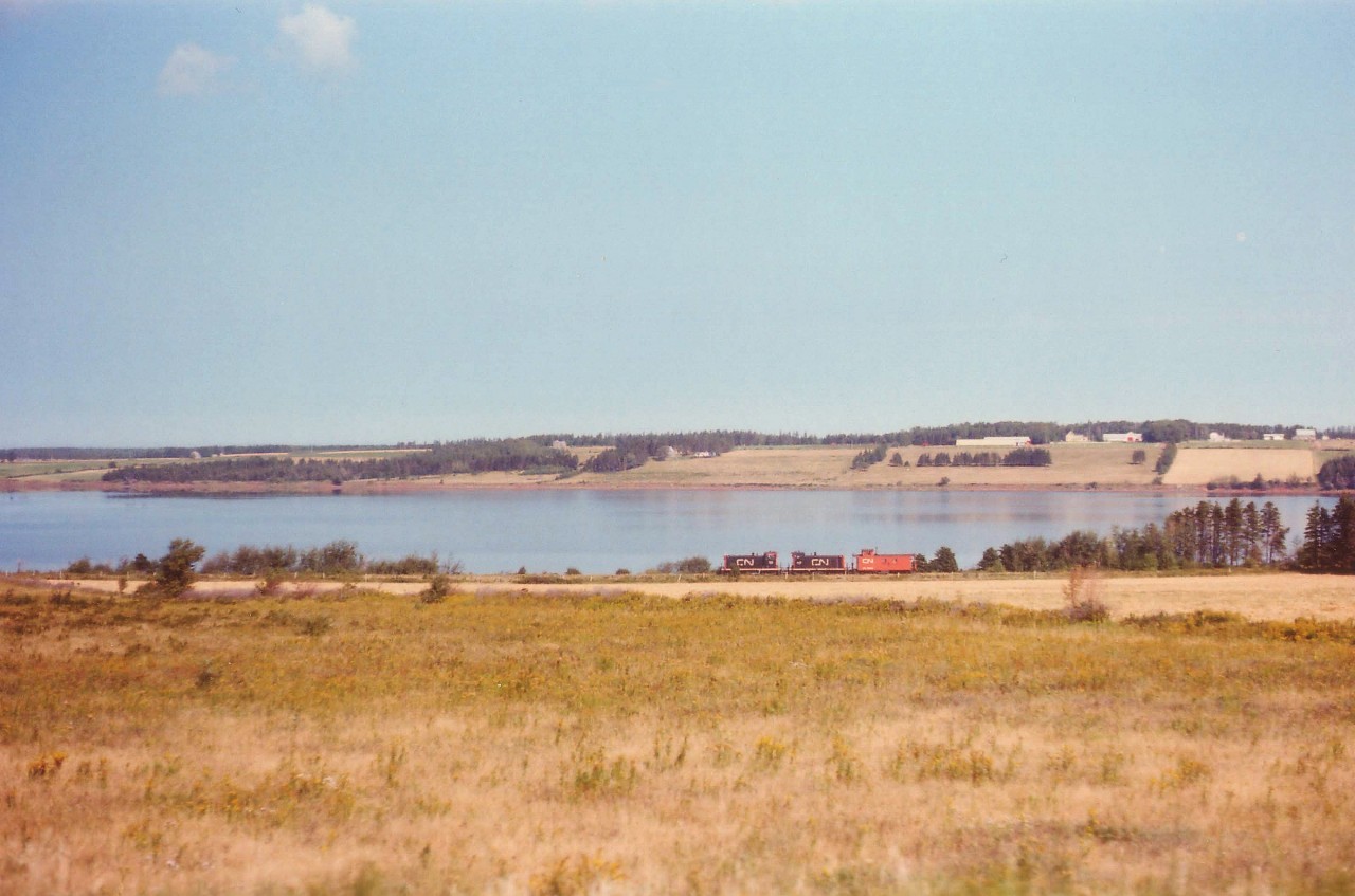 When it comes to spectacular scenery, it is almost impossible to compete with the West. However, the quaint countryside of Prince Edward Island is complimented by this equally quaint CN caboose hop rolling westward past the blissful background of St. Peter's Bay. CN 30 and 40, a pair of 70-tonners, are returning to Charlottetown after delivering a few boxcars to Souris for the potato harvest.  
(another image: http://railpictures.ca/?attachment_id=6239  )