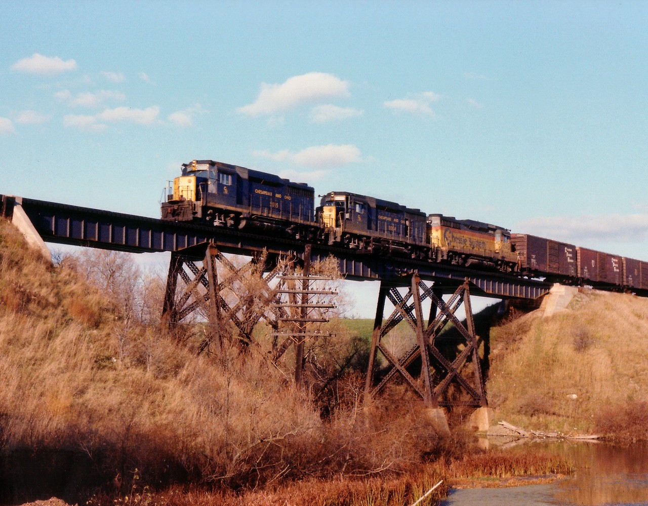 This area certainly has changed over the years. Yes, the bridge is the same and the waterway (Middle Thames River) is still there, but the runaway foliage now almost obliterates what was a great location for photos of westbounds on the CP. On a dazzling fall afternoon we see C&O 3015, 3004 and 3022 with a Canadian Pacific train approaching mile 101 west. The GP30s are of a group of 42 on the C&O roster at the time. I am assuming this is a train with run-thru power as my 'lease list'  for the early 1980s shows mostly GP38s.  Anyone with information ??