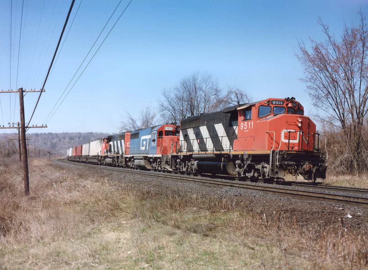 In the late 1980s for a time the CN ran something called the LASER, a dedicated daily trailer train, which I saw mostly using well cars, originating in the Toledo area, and running to Montreal. I'm fuzzy on this, so could use clarification/correction from any CN guys out there........ The service, like many othre brainstorms, didn't last long. The neat feature of this train was it was often seen with GT or DT&I power mixed in, sometimes even DT&I leading; or perhaps a set of 3 GTs!! In later years I would see it with only 2 units. This image was shot on a nice warm April morning from a favourite location on a gentle curve between York Rd and Old Guelph Rd in Dundas, lets call it Dundas Mile 1.5. I walked in from Mile 2 to park my butt here and spend a few hours. Power this day was an 'ordinary' CN 9511, GT 6400 and CN 9403.