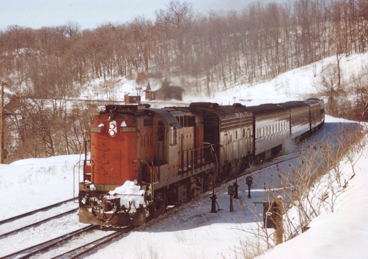 CN Tempo rolls eastward around the curve just past the old Dundas station, seen in the background. Smaller building across tracks a MoW shed, often housed 'gas buggies' when they were not in use. Both buildings  have been gone many years. On the left, old highway #8 snakes up the hill, and in the foreground two switches; one to the diminutive yard that used to be by the depot, and the closest track ran up to the Canada Crushed Stone property.  Note the old telephone box. The 3152, an RS-18m, was retired in 1983 along with its mates, 3150-3155.  Wow!! Thirty years ago as this is written. Your scribe just aged ..... thinking about this.