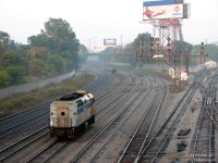 A muggy morning at Bathurst Street finds a lone VIA F40PH awaiting the 3rd track signal to head west. VIA 6412 serves as today's "drop unit" for combined J-train #40 + #52: Initially, both trains would be combined and face east at the VIA Toronto Maintenance Centre in Mimico, but they're scheduled to start their run from Aldershot Station (at 06:00) to the west in Burlington. So, instead of backing all the way there, VIA would tack on another unit on the train's rear (west end) to lead the deadhead to Aldershot, and it would then trail the train eastbound to Union Station (arriving 06:35). Before departing Union (at 06:55) the combined #40-52 would cut off the trailing unit at the station, and while the train would head east for Ottawa and Montreal, the "drop unit" would deadhead light power back to Mimico. An interesting daily movement that mingled with the GO and VIA trains of the morning rush, although today finds it waiting in a brief lull at 07:37. <br><br> (For an image of a VIA J-train, aka the combined #40-52, see here - imagine the above F40 being tacked on the rear: <a href=http://www.railpictures.ca/?attachment_id=12173><b>http://www.railpictures.ca/?attachment_id=12173</b></a>).