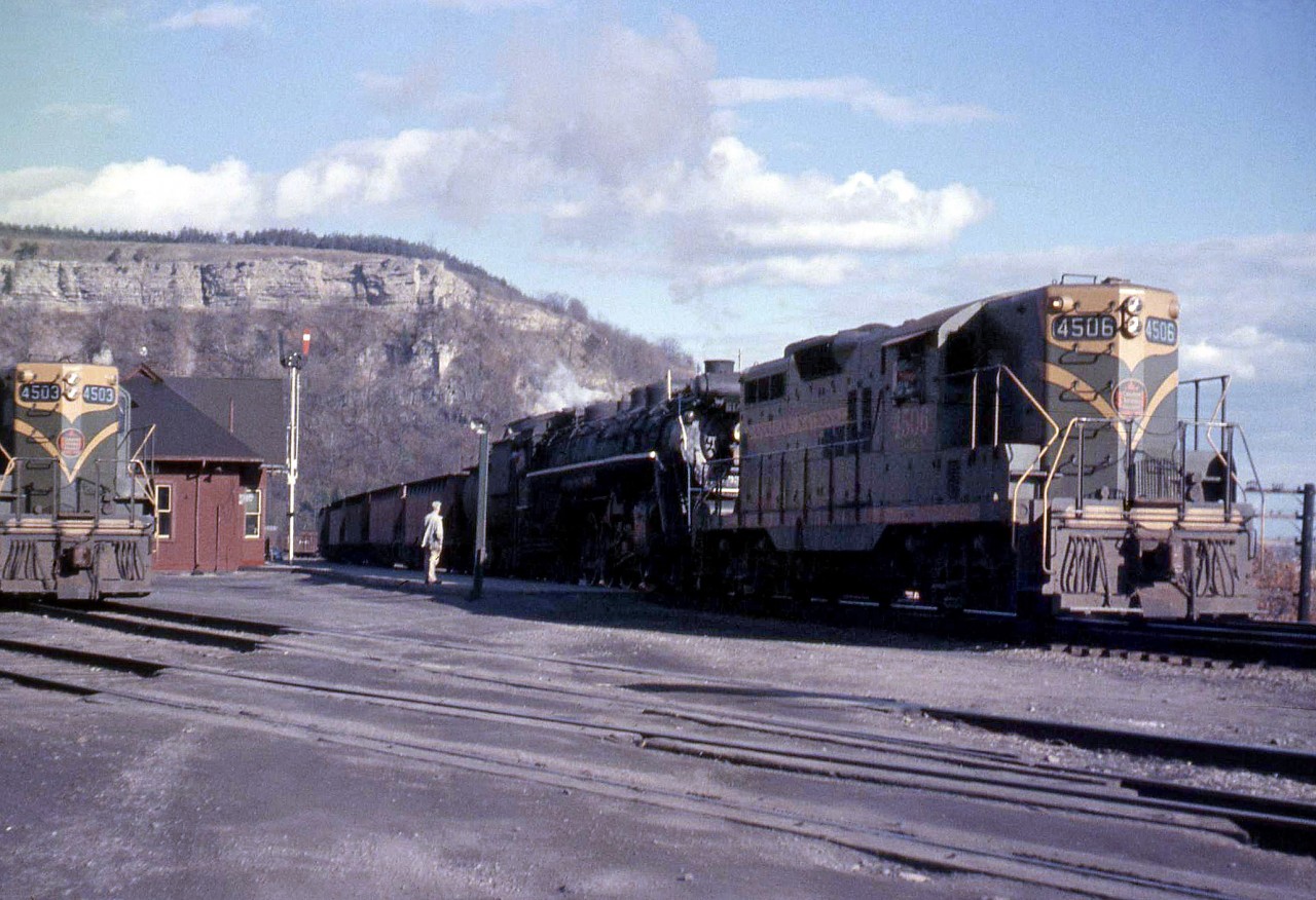 A westbound freight with CN 6189, a 4-8-4 Northern, is assisted by a relatively newer GP9 4506 as they pass by Dundas Station in 1958, with the Niagara Escarpment looming in the background. Another sister GP9 not more than a few years old, 4503, rests on the tracks by the station.