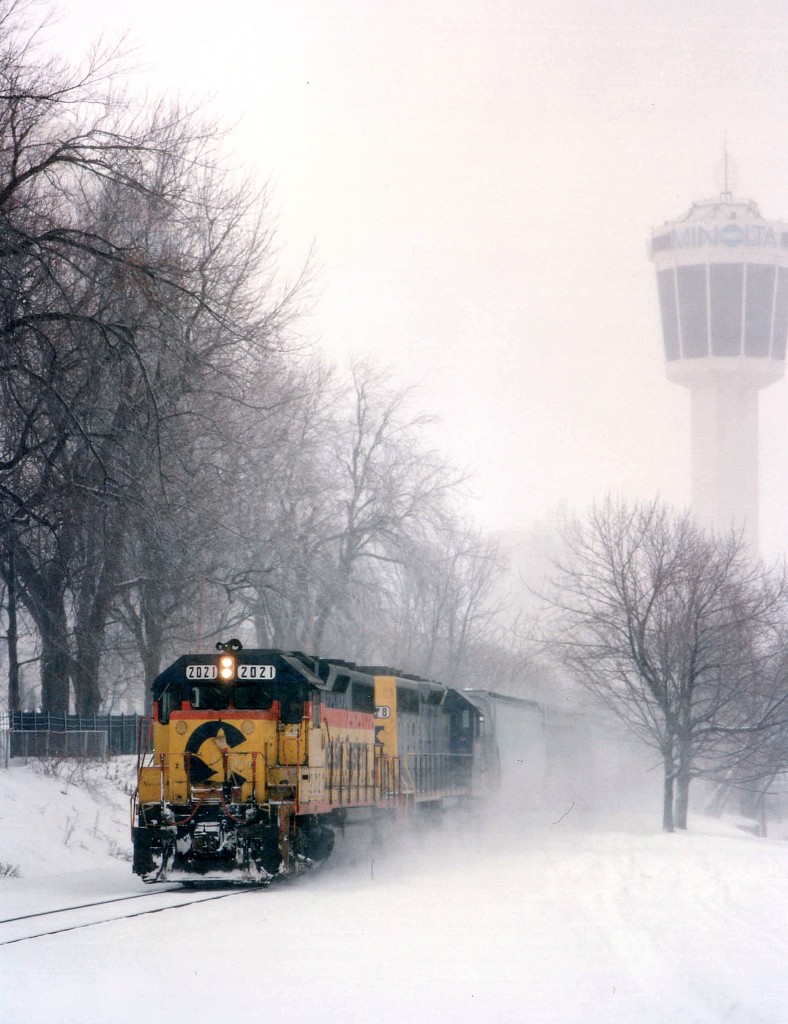 Only a few months to go!!  CSX's tri-weekly service thru Southern Ontario was going to be history by March of 1996. Traffic had been withering away and there was no money to be made. The railroad ran two trains, one each way, on Mon-Wed-Fri. West was #321 and eastbound #320. Route was CP west to Welland where they picked up the CASO. Meets often had at Hagersville. In this wintery view, CSX 2021 and 8178 power a dozen cars thru the snow, approaching the South Siding Switch, Montrose. The mainline thru "the Falls" has been taken up, but there still is track from the present-day Hamilton sub as far as the switch here that enables the CP switchers from Welland Yd.  to travel down which is now the Montrose Sub onto the Chippawa Lead to service local industry. The Minolta Tower in the background these days can barely be seen, surrounded by hotel development along the tourist strip.