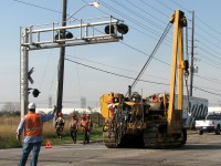 <b>Send in the Troops</b> <br><br> Things usually run smoothly on the railway, but occasionally a wrench gets thrown in the wheels. In this case, that wrench was a dozen freight cars that jumped the track on a CN 384 as it headed through the crossovers at Goreway, tieing up CN's main east-west line at the doorstep of their major Ontario intermodal terminal. <br><br> Most railway cleanup these days involves a combination of railway personnel and contractor equipment, and today there was plenty of both: more hardhats than you could shake a stick at, and a good number of Hulcher and CN trucks, cranes, and heavy machinery on site. As police stop traffic on Goreway Drive, a CN employee directs a Caterpillar sideboom tractor into position on the railway crossing, being careful to avoid hitting the crossing signal bridge with its boom. About the size of a D7 bulldozer, medium-sized sideboom tractors are popular cranes for railway cleanup applications, and this one has all the usual hooks, ropes, chains, slings, and even cutting torch tanks on the front. The "Catskinner" will maneuver her onto the north track, and head west along the railway tracks to help another tractor right the derailed cars. <br><br> Red-hatted employees from rail cleanup contractor Hulcher are also pictured, heading to the derailment site, along with CN's Mobile 1 command post trailer stationed in the background. Combined efforts would see the line opened for limited rail service the next day.