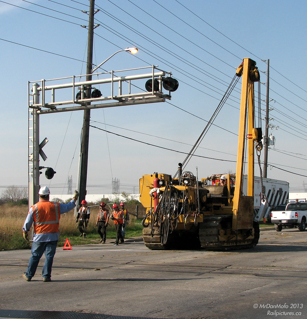 Send in the Troops  Things usually run smoothly on the railway, but occasionally a wrench gets thrown in the wheels. In this case, that wrench was a dozen freight cars that jumped the track on a CN 384 as it headed through the crossovers at Goreway, tieing up CN's main east-west line at the doorstep of their major Ontario intermodal terminal.  Most railway cleanup these days involves a combination of railway personnel and contractor equipment, and today there was plenty of both: more hardhats than you could shake a stick at, and a good number of Hulcher and CN trucks, cranes, and heavy machinery on site. As police stop traffic on Goreway Drive, a CN employee directs a Caterpillar sideboom tractor into position on the railway crossing, being careful to avoid hitting the crossing signal bridge with its boom. About the size of a D7 bulldozer, medium-sized sideboom tractors are popular cranes for railway cleanup applications, and this one has all the usual hooks, ropes, chains, slings, and even cutting torch tanks on the front. The "Catskinner" will maneuver her onto the north track, and head west along the railway tracks to help another tractor right the derailed cars.  Red-hatted employees from rail cleanup contractor Hulcher are also pictured, heading to the derailment site, along with CN's Mobile 1 command post trailer stationed in the background. Combined efforts would see the line opened for limited rail service the next day.