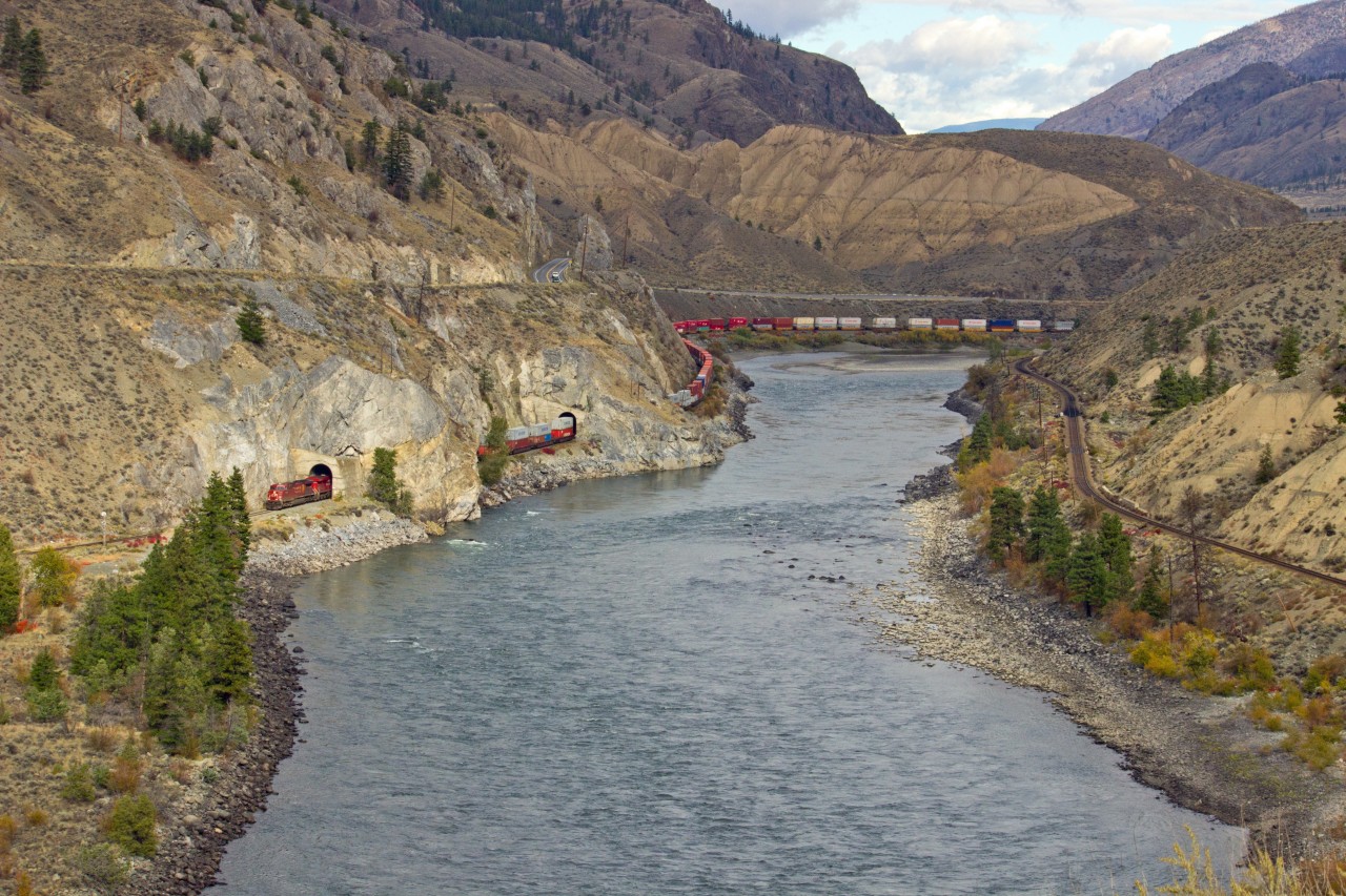 Westbound C.P.R. container train on C.N.R. Mainline. in Thompson River Canyon.  C.P.R. mainline on right side of river, Trans Canada #1 Highway above on left. C.P.R.and C.N.R. share tracks in Thompson and Fraser Rivers Canyons, west on C.N.R. and east on C.P.R.