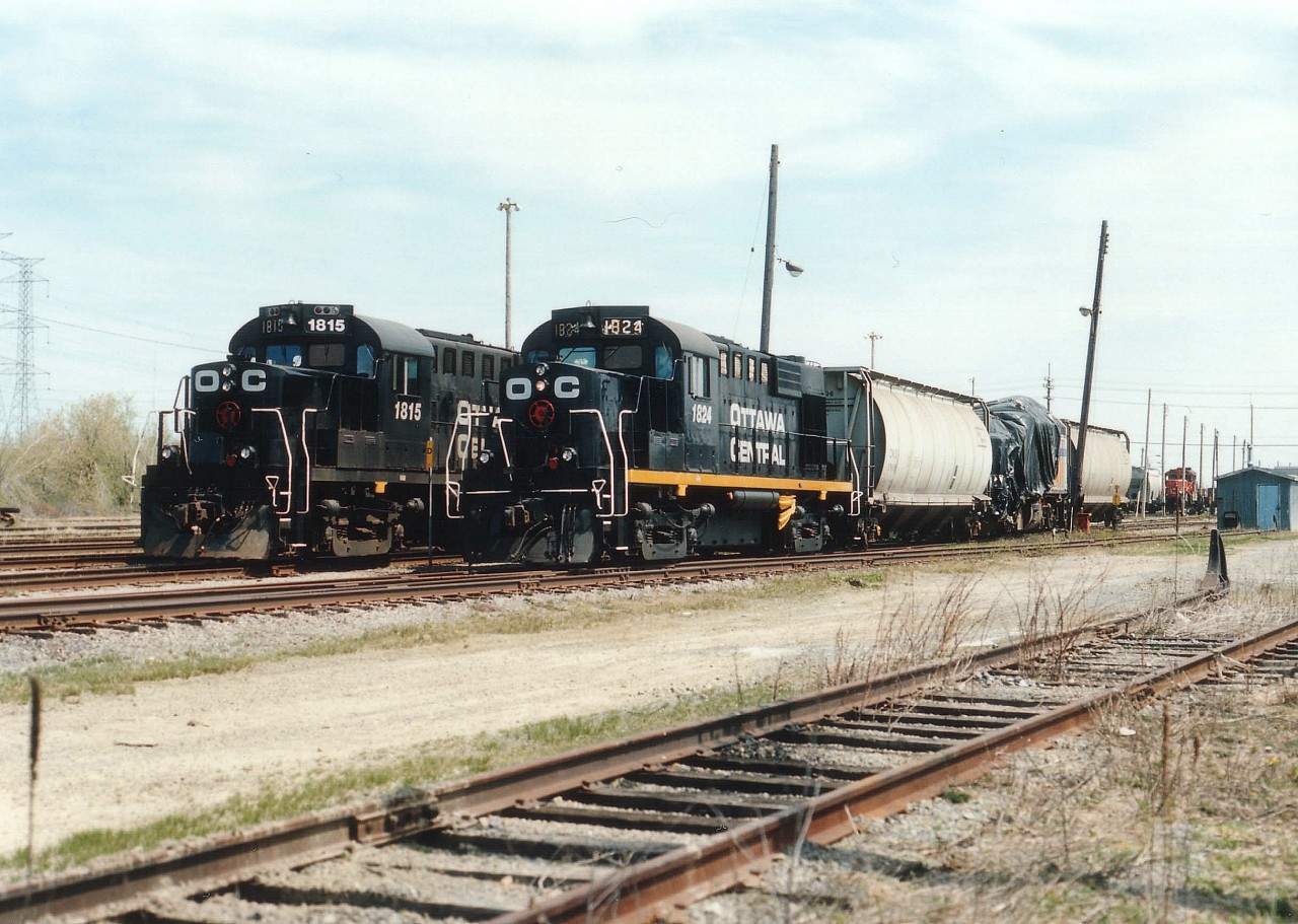 Two x-CP RS-18u locomotives of the Ottawa Central, 1815 and 1824, one with reflective stripe and one without, sit near the office in Ottawa's Walkley Yd. This railroad had a rather short history. It began on Dec. 13, 1998 as a wholly owned subsidiary of the Quebec Rwy Corp., was taken over by CN on Nov. 3, 2008 and now is a subsidiary of CN. The old CP units, which retained their numbers when relettered to OCRR, have been dealt off and now just CN power can be found here. So, thats it. Ten years. Short life. Interesting too in this image is the tarp-covered VIA unit behind the 1824. This is the 6423, wrecked at Thamesville, ON Apr. 23rd of 1999. It was hauled to Ottawa for a going-over by government inspectors as to how and why it destructed as it did under severe impact. When I walked over for a closer image of the VIA, a yard crew came out of the office, got into the 1824 and proceeded to move the locomotive down the line between rolling stock so that further photos of the unit were not possible. Perhaps the engine had just been brought to the yard, or perhaps orders were to "hide it" from nosy railfans. I'll never know for sure.