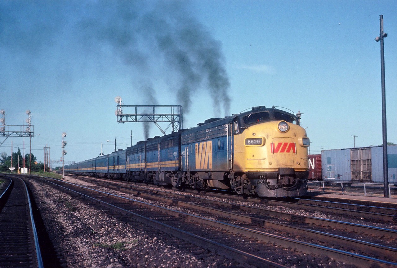 The "dinner hour" VIA #75 is seen here accelerating away from the old Burlington West station with the typical long train of the day. Power is VIA 6529, 6865 and 6634. Track on the left is the beginning of Halton Sub.