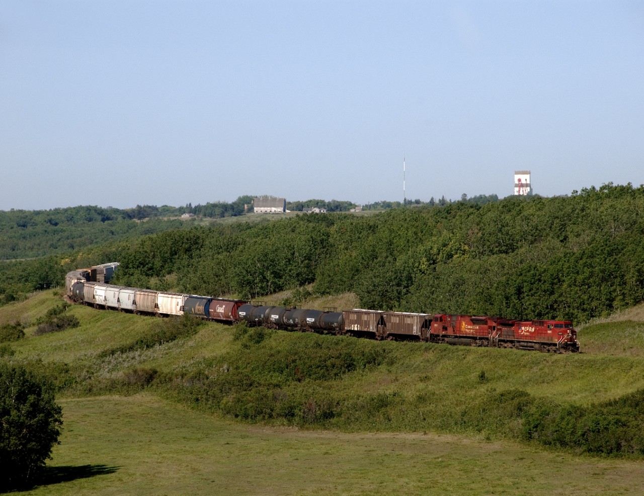 Eastbound mixed freight 454 on CP's North Main drops into the Birdtail River Valley just east of Birtle, elevators above 1st unit. This is one of 3 steep valley crossings on the Bredenbury Subdivision sometimes referred to as Manitoba's mountain railroad.