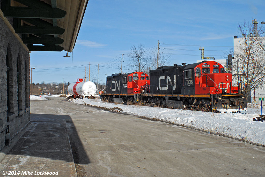 Framed by Port Hope's classic 1850's era Grand Trunk cut granite station, CN 7039 and 7000 have completed swapping out one inbound tank for one outbound at Cameco. All that remains for the crew is to tie onto the outbound and push east to the small yard at Cobourg, where they'll will go off duty and taxi back to Belleville. 1453hrs.