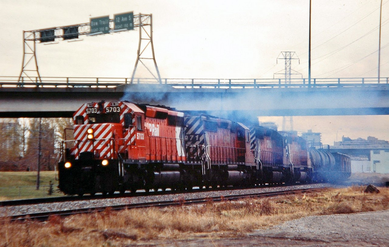 Four Multimarks headed by CP 5703 are making a lot of smoke as they pass underneath the Crowchild Trail freeway on their way westwards out of Calgary with a mixed freight.