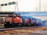 Four Multimarks headed by CP 5703 are making a lot of smoke as they pass underneath the Crowchild Trail freeway on their way westwards out of Calgary with a mixed freight.