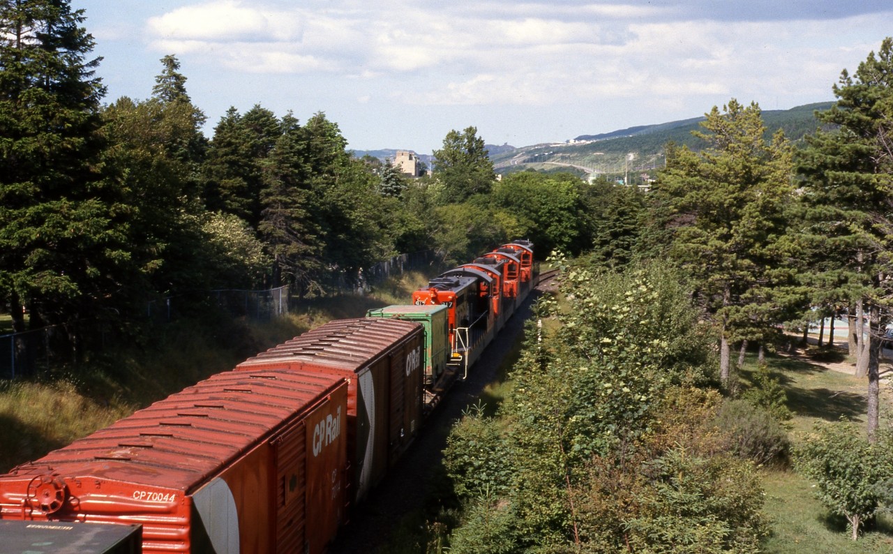 EAST MEETS WEST ON THE ROCK. TerraTransport Extra 926 East (formerly Train # 204) runs downgrade through Bowring Park in St. John’s on a hot Sunday afternoon in July 1987. The photographer was crossing the bridge at just the right time to witness this unique train. With rarely seen CP Rail boxcars and the green TT containers, both coasts of Canada were well represented in this particular consist. This photo and it's contemporary update along with many others can be seen in 'RAILS ACROSS THE ROCK - A Then & Now Celebration of the Newfoundland Railway' by Kenneth G. Pieroway and published by Creative Book Publishing of St. John's, NL. – Author photo.