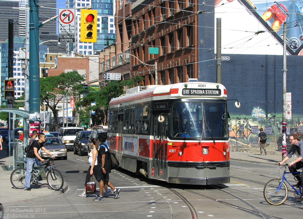 Hustle and bustle of the city streets on a warm summer's day. With pedestrians, cyclists and cars going about their merry way, TTC CLRV 4061 waits to make the turn onto Spadina Avenue from King Street. While some runs of the 510 go to the end of the line at Union Station via Queen's Quay, a number of 510s turn at King and head back up Spadina, to the street's namesake station at Bloor.