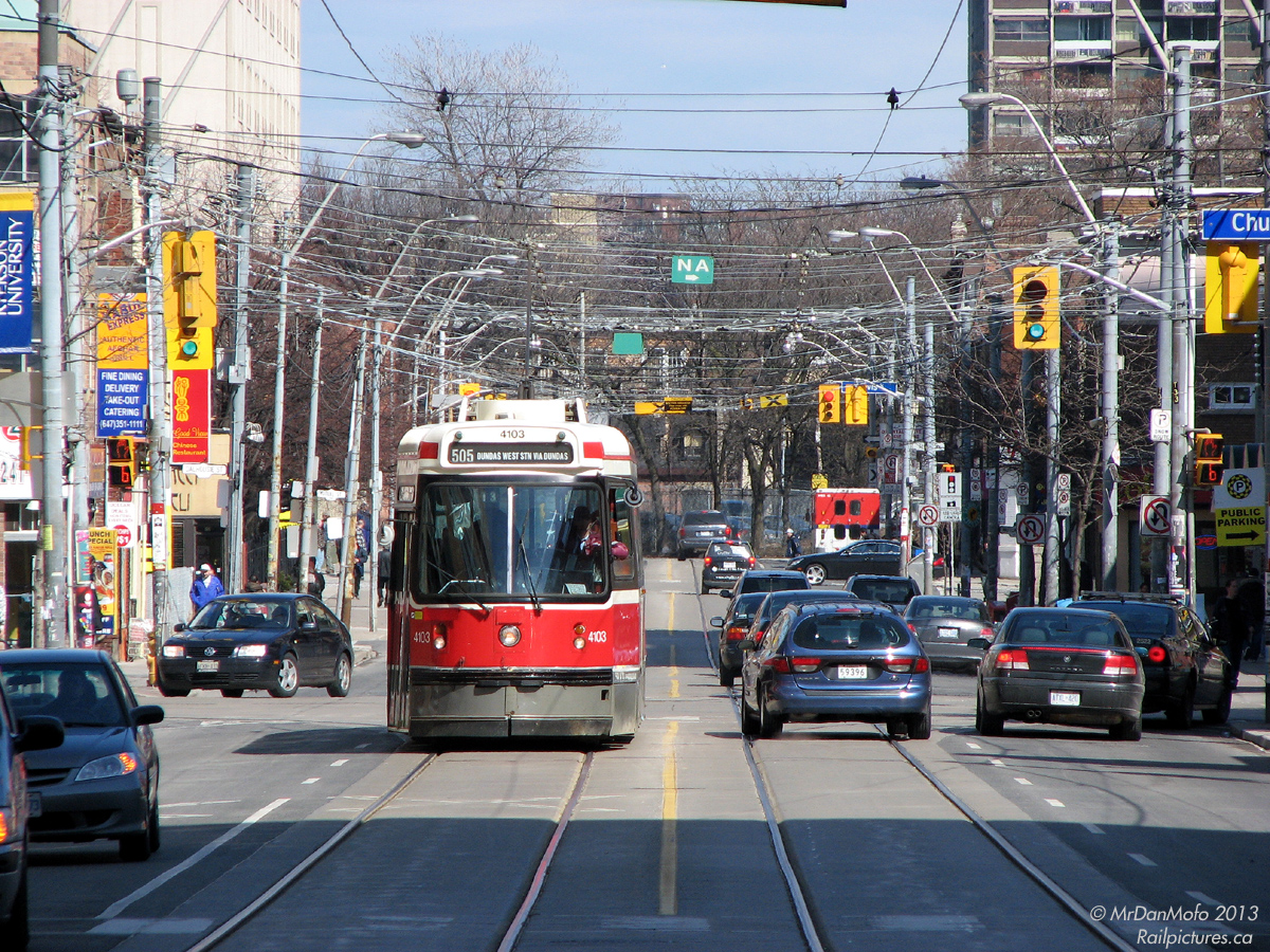 Rolling through the sunny streets of downtown Toronto, TTC CLRV 4103 cruises westbound along Dundas Street after stopping at Church. Traffic, both on rubber soles and and on rubber tires, goes about its late afternoon business.

It's amazing in a way all the different areas and neighbourhoods a streetcar in Toronto can pass through from one end of its route to the other; take this particular section of the 505 for example. While the ever bustling and commercialized Dundas Square is behind us along with the Eaton Centre, and further to the west there's lots of suit spillover from Bay Street and University Avenue, the kink in Dundas after Victoria and the tall buildings isolate this quieter section of Dundas nicely. Calmer and less busy, the stores lining both sides see a moderate amount of foot traffic from the neighbouring Ryerson University and its residences. Another curve in the distance arcs Dundas St. to Sherbourne, and through the more seedier neighbourhood of Moss Park. Generally safe during the day, once you pass Filmore's Hotel just around the bend it's best to proceed with caution all the same, and use discretion when walking around with a camera.