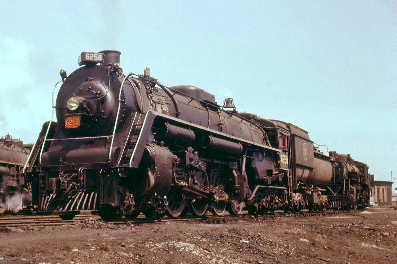 Canadian National 4-8-4 6258 rests among other steam engines at the Mimico roundhouse in 1956. One of CN's large fleet of Northerns, 6258 was built by MLW as part of the U2h-class in 1944, making it just 12 years old when this photo was taken. CN was ordering brand new GP9's and RS10/18's at this time, and the end of steam was not far off: 6258 would be scrapped 5 years later in 1961.Located in the town of Mimico (now an inner suburb of Toronto) and just to the south of the busy Oakville Sub, the Mimico roundhouse would be demolished in the 60's, the turntable removed and the pit filled in. Presumably this occurred when CN moved its locomotive servicing to the new Toronto (MacMillan) Yard and its more modern diesel repair facility. Today VIA and GO Transit have large servicing facilities in Mimico, but CN's presence here is but a shadow of its former self: a small freight yard to serve the few remaining local customers that use rail.[Historical Editor's Note: VIA has a turntable here at their Toronto Maintenance Centre, but it's located in a spot northwest of where the Mimico Roundhouse's turntable would have been. It is unknown if this was a brand new turntable, or if the old Mimico turntable was available and reused in a new pit.]