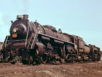 Canadian National 4-8-4 6258 rests among other steam engines at the Mimico roundhouse in 1956. One of CN's large fleet of Northerns, 6258 was built by MLW as part of the U2h-class in 1944, making it just 12 years old when this photo was taken. CN was ordering brand new GP9's and RS10/18's at this time, and the end of steam was not far off: 6258 would be scrapped 5 years later in 1961.<br><br>Located in the town of Mimico (now an inner suburb of Toronto) and just to the south of the busy Oakville Sub, the Mimico roundhouse would be demolished in the 60's, the turntable removed and the pit filled in. Presumably this occurred when CN moved its locomotive servicing to the new Toronto (MacMillan) Yard and its more modern diesel repair facility. Today VIA and GO Transit have large servicing facilities in Mimico, but CN's presence here is but a shadow of its former self: a small freight yard to serve the few remaining local customers that use rail.<br><br>[<i>Historical Editor's Note: VIA has a turntable here at their Toronto Maintenance Centre, but it's located in a spot northwest of where the Mimico Roundhouse's turntable would have been. It is unknown if this was a brand new turntable, or if the old Mimico turntable was available and reused in a new pit<i>.]