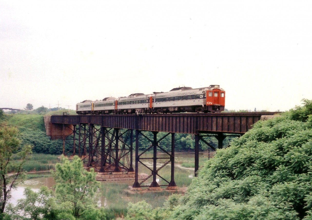 A set of four BuddCars are seen Toronto-bound from Niagara Falls at the rarely photographed Sixteen Mile Pond bridge; one which is vastly overshadowed in popularity by the larger bridge at Jordan Harbour. This location is not visible from the roadway, and is off-limits as to private property on both sides. VIA passenger service has been discontinued along this route. Only Amtrak prevails, plus of course, a couple of morning freights each way.
