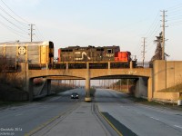 Shuffling around racks to be loaded with brand new automobiles at the sprawling Ford assembly plant complex in Oakville, CN GP9RM 7007 crosses over the concrete arch bridge spanning Royal Windsor Drive in the evening. <br><br> One of the two bridges for the switching leads into the plant from CN's nearby Oakville Yard, the abutments on this one are stamped 1952, dating back to the construction of the plant in the 1950's.
