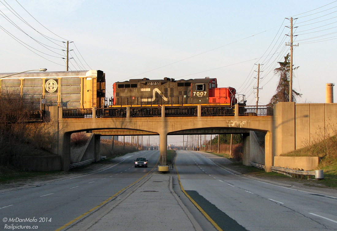 Shuffling around racks to be loaded with brand new automobiles at the sprawling Ford assembly plant complex in Oakville, CN GP9RM 7007 crosses over the concrete arch bridge spanning Royal Windsor Drive in the evening.  One of the two bridges for the switching leads into the plant from CN's nearby Oakville Yard, the abutments on this one are stamped 1952, dating back to the construction of the plant in the 1950's.