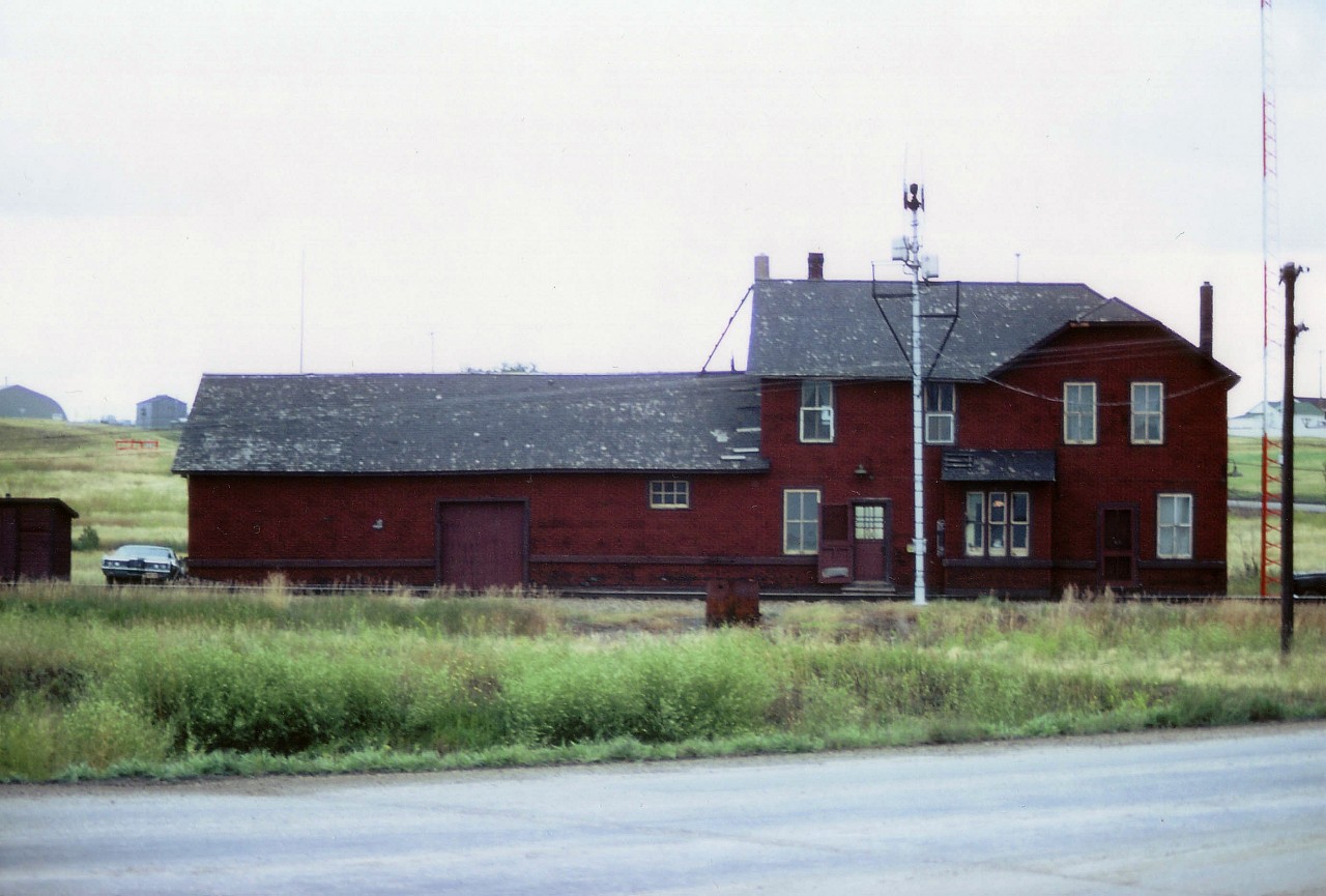 To me, the beauty of this station is the sheer ugliness of it. Big wooden structures like this weary dive with its layer of "phoney-brick" and drafty windows were scarce even back in the '70s. Living quarters upstairs must have been hell to heat in the windy wild winters of southern Saskatchewan. No doubt when this photo was taken, the structure, with its huge freight section, was close to falling down, blowing down or torn down. But still, as in many other lonely railroad buildings through-out the prairie, the light was on, and the agent was home.