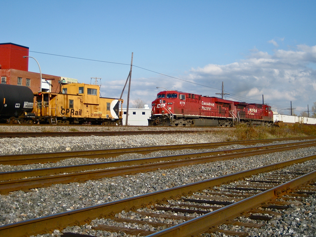 Modern railroading blows by the old. Representing modern railroading, a CP westbound with two modern, widecab GE's (CP 8775 & CP 9561) and a long string of intermodal cars blows by a caboose (CP 434957) which is stopped and at the tail end of the Dorion Turn which has a GP9 (CP 8228) and 5 cars ahead of the caboose. For more train photos, click here.