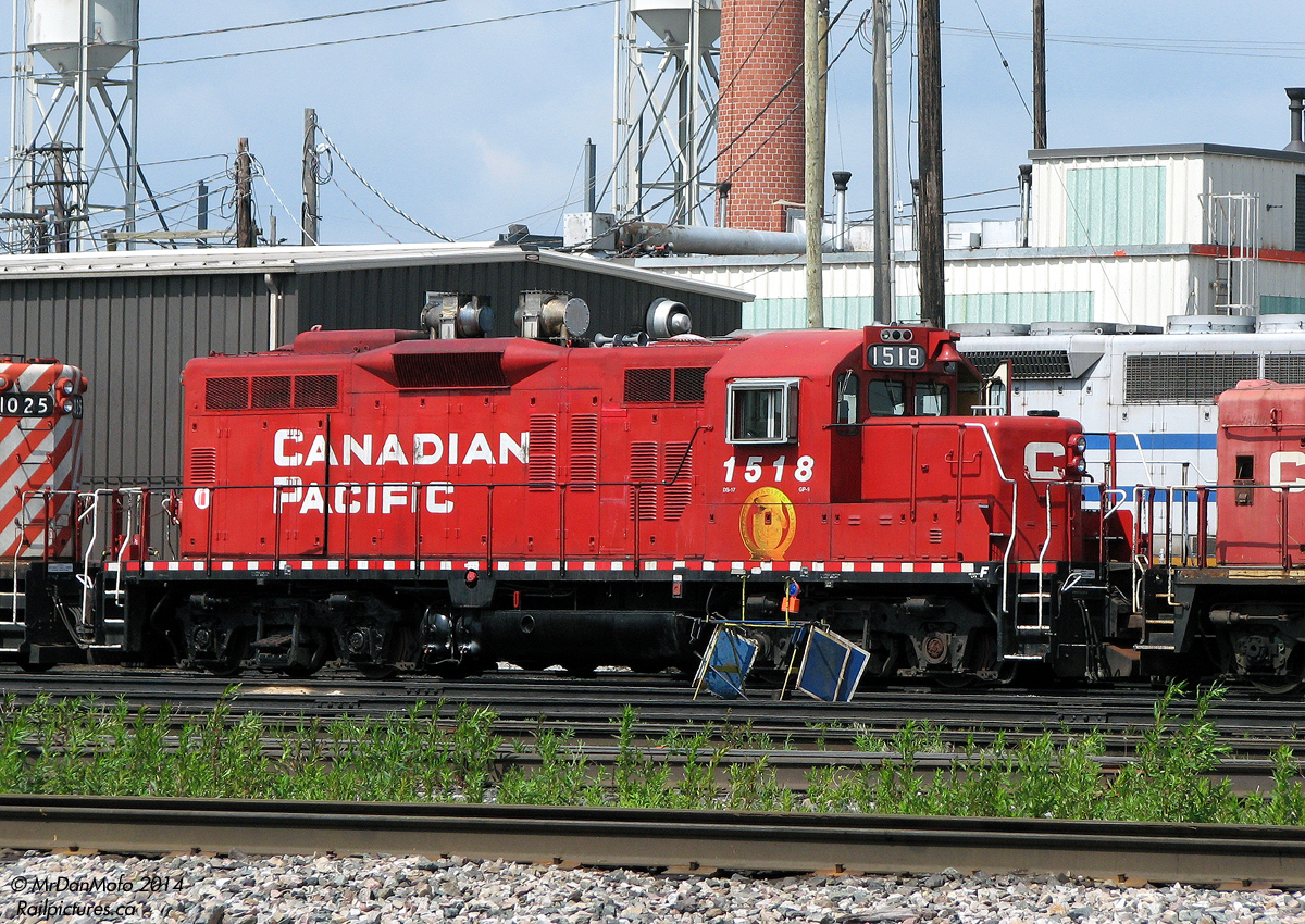 Odd Duck. CP GP9u 1518 sits at the diesel shop in CP's Toronto (Agincourt) Yard on a sunny day in shiny CP beaver paint. One of the early 80's GP9 rebuilds for yard service, 1518 was later equipped with two spark arrestors on her roof for switching inside the GM Oshawa automotive assembly complexes. She is also a "mother" to slug 1025 (coupled behind), another former GP9u (1534) that was converted to a slug in the early 90's after suffering an engine failure.  The ECO craze retired both, with 1518 and 1025 tied up unserviceable at Toronto Yard in December 2013, and unlikely to return to service or see a second life on a shortline.