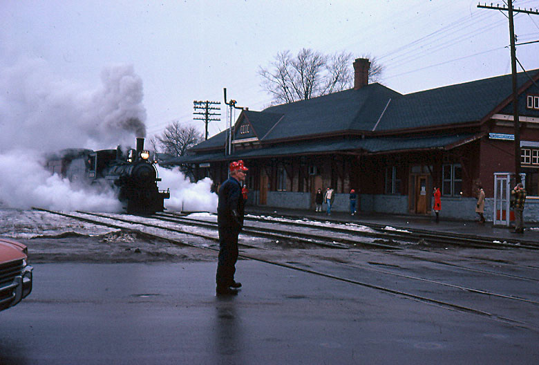 Former CP 4-4-0 136 gets flagged across George Street on a dreary warm March day. 136 and a train of two cars with people in period clothing were being filmed by a CHCH tv crew for a Christmas special by the Dofasco choir.