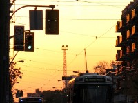 After taking on passengers, TTC CLRV 4133 pauses at the lights of King and Strachan before continuing on a 504 King run for the downtown core, in the gentrified and hip King West neighbourhood. <br><br> Once lined with garment factories and heavy manufacturing industry like the Toronto Carpet Factory and Massey Harris's equipment manufacturing plants (later Massey Ferguson), the departure of industry in the 80's and 90's coupled with the desire to live downtown saw this area along King Street converted from heavy industrial to commercial and residential use. Old factories were torn down for new condos and townhouses, with some older historic buildings repurposed into offices, lofts and residential units. The connecting route 63 bus behind 4133 will turn down Strachan for the trendy Liberty Village, to service streets that people once went to work along but now come home to. All the new residents in this area consequently have put a strain on transit, and the King streetcars are often packed to the doors during rush hour. <br><br> Another casualty of this gentrification can be seen looming in the background like a beacon in the sunset: one of the lighting towers for CPR's now-removed Parkdale Yard, sitting abandoned with nothing more to light. Time turned Parkdale Yard into townhouses, office buildings and retail outlets, as when all the rail-shipping industry moved out, so too did the need for a rail yard to serve them. 