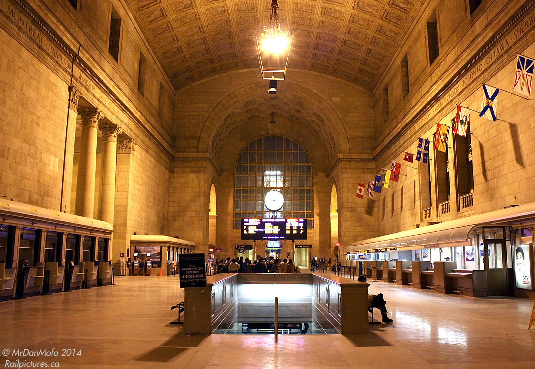 Just a quiet evening in the Great Hall, in downtown Toronto's Union Station. People departing on or arriving off trains congregating together, others buying tickets on late night departures at the VIA ticket wickets. Some sitting around waiting for their ride, be it a train or an automobile, others (like the photographer) enjoying a quiet moment before catching their GO bus home. The names of cities across the country adorn the 1920's stone walls near the high arched ceiling, and flags of the provinces and territories of Canada lining the north wall flap lazily with the odd wisp of air. All is quiet, all is calm. 21:13hrs.