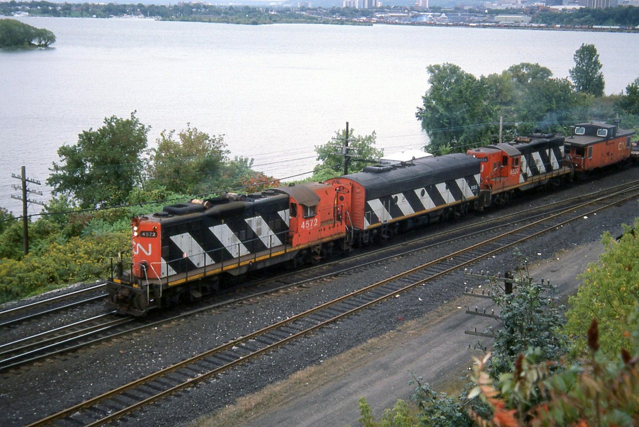 CN GP9's 4572 and 4520, braketed by a CN F7B (likely 9196) handle the Steel Train at Bayview Junction on the Hamilton/Burlington border. By this time, the train was now using the Dundas Sub to Brantford and then down to Nanticoke. In the background is Hamilton Harbour, where CN's Hamilton / Stuart St. Yard is visible (where the Steel train originated), along with various industries and manufacturing plants located nearby.