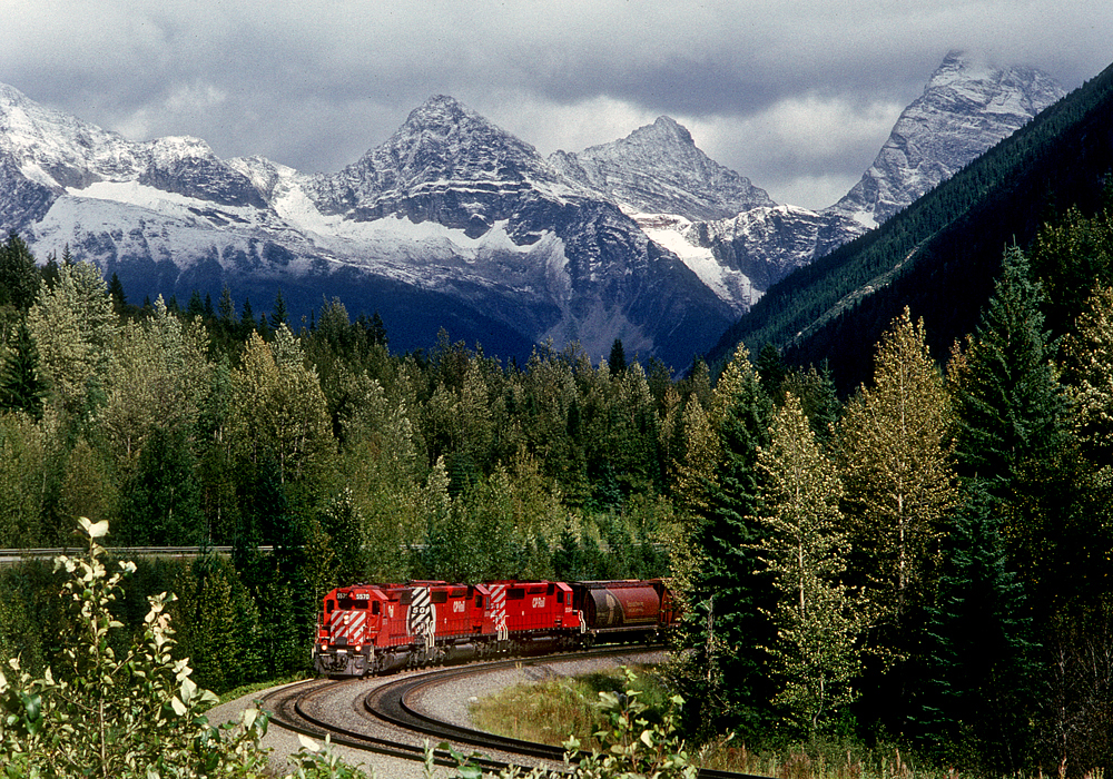 Westbound just west of Rogers Pass.  We were driving west, not far ahead of the train, when we saw this kind of lighting in the rear view mirror.  We quickly pulled off the road, jumped out of the car, and looked for a shot.  Unfortunately there were a bunch of bushes in the way.  But by standing on the tip of my toes I could barely shoot over the bushes.