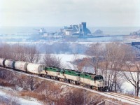 Interesting town, is Goderich.  In a photo taken around 2 years after startup of the GEXR, we see three of the original four locomotives hard at work bringing heavy loads of salt up to the yard from the Sifto Salt Mine on Lake Huron (seen in background)in order to build a train to deliver to Stratford. It is a warm day, as evident by the mist, making it difficult to see the long string of salt-laden hoppers in the left background, just in front of the lake freighter at the  salt dock. Old track line in mid-background is former CP Goderich line, now reduced to a hiking trail. Photo shows GEXR 177, 178 and 179 sharing in the struggle up a rather steep grade, 
Fourth unit in the stable, 180, is nowhere to be seen.  The salt mine, incidentally, is the largest in the world. There is so much salt down there 1750 meters down that the mining area consists of 7 sq kms below the lake and the vein stretches as far as Cleveland and Detroit to the south. Long ago a tropical sea occupied this part of the world, and when the sea disappeared, the salt was left behind.