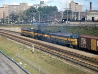 Sunnyside flashback: long before shiny new GO MP40's hauling 12 car trains hustled back and forth along this corridor, a CN freight with three Ontario Northland units as power (ONT FP7's 1507 and 1511, sandwiching RS3 1305) heads westbound through Sunnyside in Toronto, back in October 1964. They're hauling a freight train bound for CN's large Mimico freight yard, before CN moved most of its operations to MacMillan yard and GO and VIA took over. In the background shiny maroon and cream PCC streetcars sit outside the TTC's Roncesvalles Carhouse, and further down the The Queensway stands St. Joseph's Hospital (Health Centre today). Part of the CN Sunnyside Station platforms are visible in the lower right, and in the lower left is the Gardiner Expressway, not yet 10 years old.