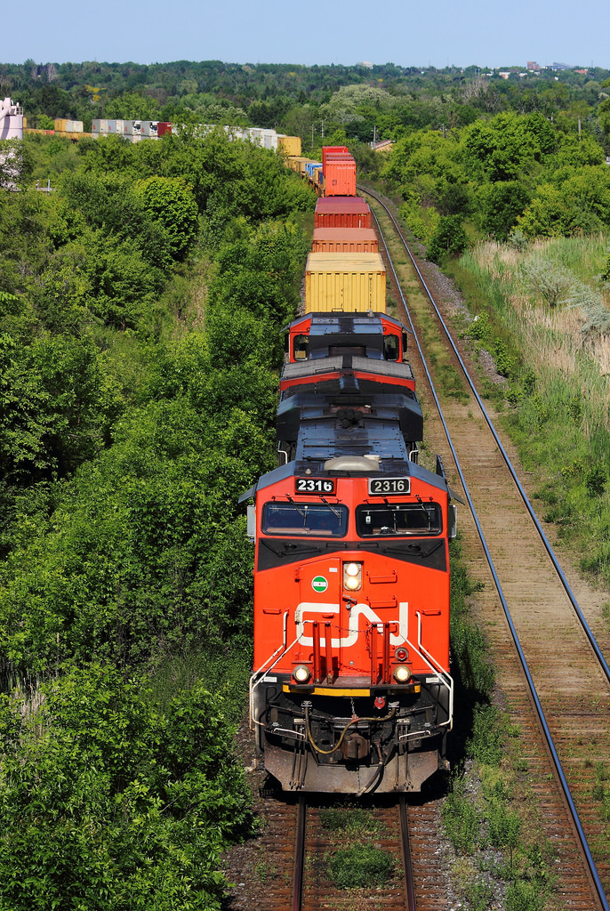 In this photo, CN 149 makes it's way through one of the nicest curves on the CN York Subdivision at Yonge St. This is my first time at this bridge with the trees blooming, and I think this will be a location I will be visiting many more times in the future.

For comparison, here is a shot in the same location about a month before this one was taken. What a difference!

https://www.flickr.com/photos/skyrailproductions/13978222657/in/photostream/

This photo is one of the first I have uploaded in a few months. I'm glad to be back and posting to the site after such a long time. I hope to be uploading many more photos soon.