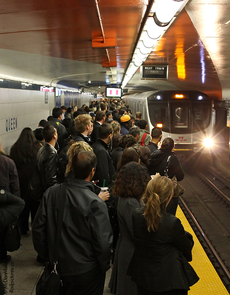 Hoards of rush hour passengers crowd the platform at Queen Subway Station, as their northbound train arrives in the station. Due to slower door cycling, the new Bombardier "Toronto Rocket" subway cars tended to create service gaps along the line, and the cause of this slightly larger-than-normal crowd is evident as one rolls into the station. Naturally it was already packed onboard, and two trains had to pass before the photographer could squeeze into one for the trip up the line to Bloor station, crammed in like sardines and standing elbow-to-elbow with everyone else that managed to squeeze in.

A downtown relief line would be nice, future Toronto mayoral candidates...hint hint.