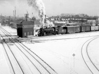 Steam-era West Toronto Diamond in the Winter: Canadian National Mikado 3518 heads north on the Brampton Sub (today the GO Weston Sub), passing the former West Toronto interlocking tower and about to cross the diamonds with the CP's North Toronto Sub. A group of employees tend to the ten(!) diamonds that make up this interlocking. In the background on the left one can spot the CP grade crossing tower for Osler Avenue. On the right, the tracks of the CP Galt Sub curve under the now-demolished Old Weston Road bridge where this photo was taken from. <br><br> The large human-manned interlocking tower here locally controlled the passage of CN & CP trains over each others' tracks, and was demolished around when the interlocking plant was upgraded to be remotely control by the CP Toronto Terminal RTC around 1965 (photo of the area soon after <a href="http://www.railpictures.ca/?attachment_id=15874"><b>here</b></a>). In May 2014, the final train crossed the diamonds here - after years of construction work, GO Transit/Metrolinx converted the diamonds to a fly-under to reduce delays for increasing passenger service on this corridor. <br><br> The closest pair of diamonds are for the CP Galt-MacTier connecting track, allowing trains like The Canadian heading to and from nearby West Toronto Station to get onto the MacTier Sub (shown <a href="http://www.railpictures.ca/?attachment_id=7371"><b>here</b></a> by James Adeney using the connecting track). It also crossed over both tracks of the Brampton Sub out of frame to the left via two more diamonds. The next two tracks are the afforementioned CN Brampton Sub mainline from downtown Toronto to Brampton, Guelph and beyond (later becoming the Weston Sub, today owned by GO Transit). <br><br> The last track crossing just behind the tower is CP's "old Bruce" service track to industries on the east side of the corridor, heading as far down as Laura Secord (Nestle today) at Dundas Street before connecting with CN near Parkdale. It was part of the original Toronto, Grey & Bruce line before CP absorbed it, with much of the line to the north becoming the CP's MacTier Sub. The Penfound Varnish Company on the right was also serviced off this track. This diamond crossing was eventually removed and replaced with a sharp curving lead starting by Osler Ave. The old Bruce service track was fully removed in the 90's after much of the manufacturing industry along this corridor located elsewhere or stopped shipping via local sidings. Today all the industry and customers that once shipped by rail in this area are gone, but mainline freights, passenger and commuter trains still pass through on a constant basis.