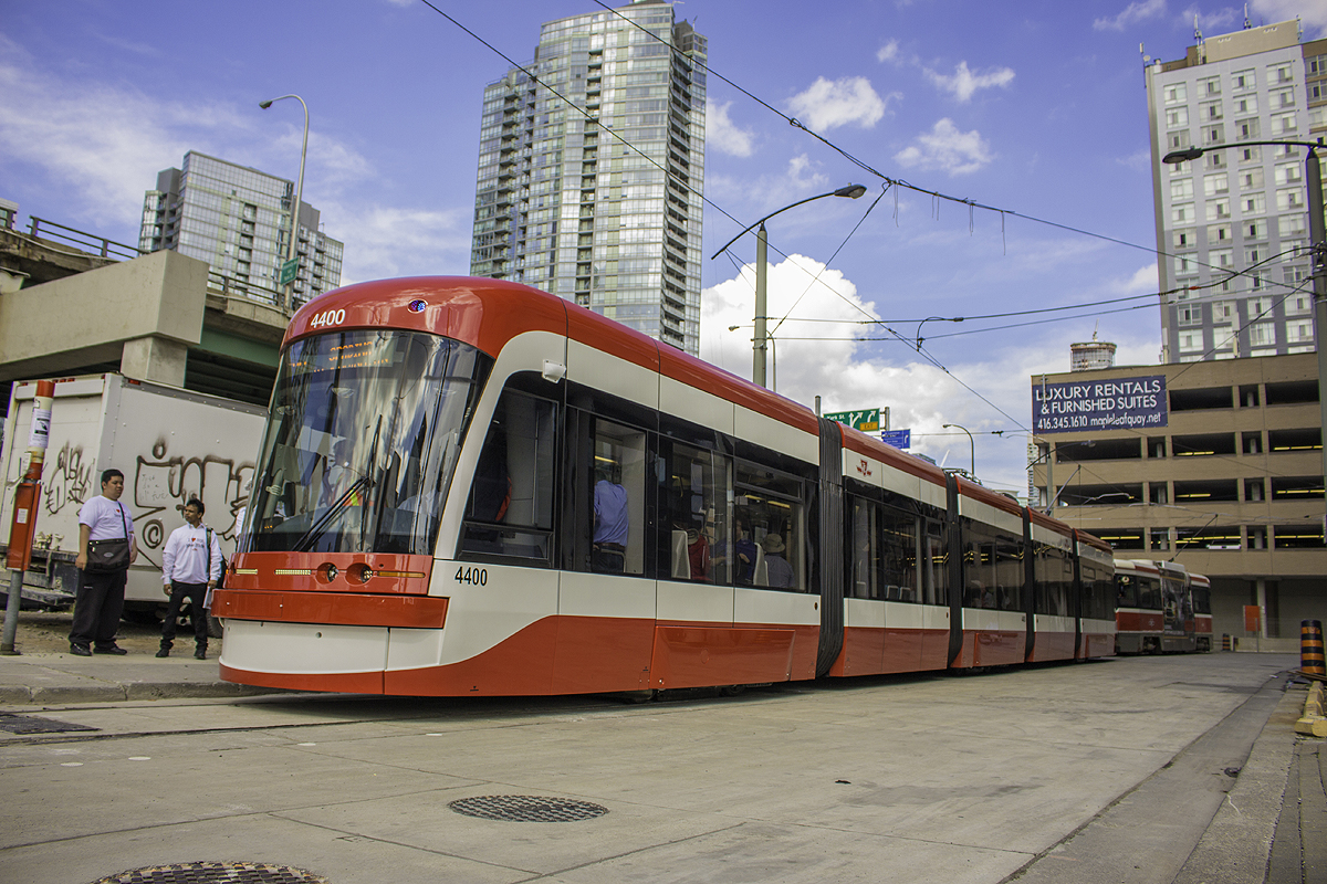 On the first day of the new low-floor Flexity streetcars in service on the TTC system, 4400 rests its bendy 5 sections at Queens Quay/Spadina Loop. I tell ya, the turnout for the only two new Flexity's in service was incredible, and passengers were so happy they gave a round of applause at Spadina Station. I almost made the first one, 4403, however I wanted to enjoy my first ride, not be a sardine. It was worth the wait, and I got a seat on 4400 to Queens Quay. Here it dwarfs a highly underappreciated CLRV behind it. One of these days, the Flexity's will just be another TTC vehicle to passengers, much like the CLRV. However, one thing I'm sure that will be appreciated is with the amount of these high capacity sets ordered, they should greatly increase overall capacity on the streetcar network. The only issue that's bothered me is the destination signs appeared to be displaying improperly on both sets that were out on Spadina, and appears to be an issue on the other two that weren't in service today. Other than that, I'll be glad to see these make their way into the system. The TTC sure picked an eventful day for the new streetcars to roll out. Just minutes after 4400 left northbound, the "ship horn" from the Rogers Centre went off with fans letting out a good roar, easily heard from Queens Quay. Meanwhile, the air show was occurring, and of course the chaotic CNE.