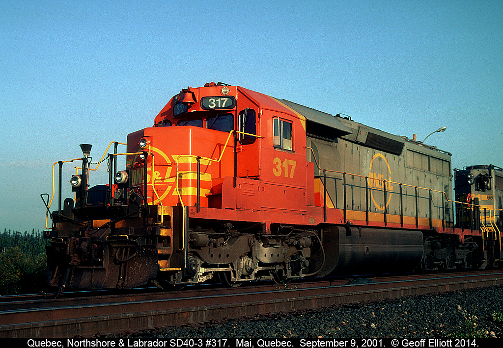 Don't bother trying to find 'Mai' on the map.  It's the name of the crew change point mid-way between Sept Isle, Quebec and Labrador City.  It's simply a small group of buildings, including a mess hall and sleeping quarters for crews.  Here QNS&L #317 sits in 6:00a.m. sun on a southbound ore train waiting for a new crew.  I wouldn't suggest you try to get here by car as there are no roads and there is nothing but wilderness and wildlife for a 100 miles in any direction!!