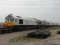 Sitting in the rain on a gloomy day, a gang of brand new JT42CWRM "Class 66" (or, Class 77) units sit at CN's Mimico Yard awaiting forwarding to the Toronto Port Authority.
<br><br>
Euro Cargo Rail 077026, 077025, 07727, 07723 with grey Crossrail DE 6312 among them are just 5 of the 9 units waiting to head overseas to Europe after being built at EMD's London, Ontario locomotive assembly plant. Moving on their own wheels, EMDX idler cars with a regular coupler at one end and buffers at the other allow regular locomotives to move them (note the "Spare hook & buffer" lettering on the toolbox). Today the EMD plant is closed, and export locomotives no longer travel through Canada to the ports in Halifax and Toronto.
<br><br>
Switch and track panels litter the yard, with the CN yard office and Lantic Sugar plants visible on the right, and the Islington Avenue overpass and a GO train in GO Transit's Willowbrook Yard on the left.
<br><br>
<i>Taken from behind the fence of an adjacent commercial property looking into the yard.</i>