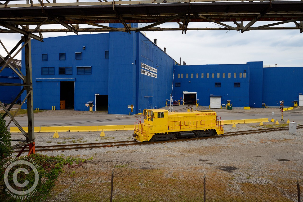 Framed in industrial pipelines and steel fencing, USS Hamilton SW900 #84 is rolling back to the inaccessible depths of US Steel's sprawling Hamilton works after having placed 9 coil cars in the building behind it. Life clings precariously to the Stelwire fence - waiting for the opportunity to once again flourish in this man made industrial world. Might not be too long either.

Much can be said about the future of US Steel Hamilton (Stelco) - the day after I took this photo United States Steel announced in a quarterly and regulatory filing their plans to cut off US Steel Canada from the parent company, and forcing receivership. As a native Hamiltonian - it's sad to see the once glorious Stelco wither - but at least I've been able to see and photograph something like this in 2014. USS bought Stelco Canada in 2007 in a bidding war against Russian conglomerate OAO Severstal - Severstal has since closed the US plants they purchased in lieu of Stelco. Essentially, United States Steel was forced to keep Stelco alive for nearly 10 years. Will it survive? If you read the media, all signs point to no - but we have to wait and see what happens - coke making licenses are not being given out in North America any longer and I suspect it will be of value to the purchaser. However, as a taxpayer, whoever wishes to continue coke making operations should be forced to continue to make steel on-site and give Hamilton economic benefit for the pollution being created, or close Coke making at USS Hamilton permanently.