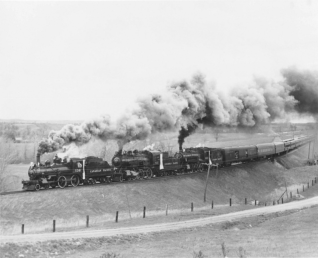 This photograph of the train running through open countryside shows the entire train of three locomotives and 14 cars! A quarter mile long and nearly 1000 tons.  The lightweight baggage car with electric generator for tape recorders and gated doorways typical for railfan excursions as well as food and drink supplies for the vendors who went though the cars.  Two lightweight air conditioned coaches with reclining seats are next. Two more were substituted for higher seating capacity heavyweight coaches more typical for a train of the steam era.  Even more seating would have been of benefit to the hundreds of people turned away. It would however have spoiled the appearance of the train so I stopped there.  Two ancient wooden coaches (1595 and 1596) brought up the tailend to represent earlier years.  These cars were brought to Toronto from The Glen Yard in Montreal along with a spare protect coach 1583.  A dining car was placed in the train to provide full meal service complete with a special souvenir menu.  The CPR wanted to add a second dining car to handle the anticipated demand however; they wanted to reduce a coach stating they didn’t feel the engines could not handle 15 cars. I refused because the loss of about 80 tickets would have meant the loss of any profit.  This was a very expensive event.   Had a third D10 (1087) been used the second diner and perhaps another coach could have been handled however the 136 was already committed to.  Besides, it would not have been the big drawing card without the little 4-4-0. 

Note the new white canvas curtains applied to the engines as the CPR went all out dressing up the engines in passenger special trim including white tyres, silver armoured cable to head and class lights as well as builders plates. Red paint inside the bells!  Even new bell ropes.  Engines and tenders were cleaned and painted, cab interiors painted CPR standard green with red trim. Too much paint in fact.  All the valves etc. were freshly repainted black BUT the CPR wanted Passenger Special trim which meant polished brass everywhere! I recall checking on the engines a day or two in advance at Lambton roundhouse where I worked and found a labourer with a big file hand filing the fresh paint off the brass valve nuts! What a job!  I quickly left the cab without saying anything before he blamed me! 

Raymond L. Kennedy CPR Retired