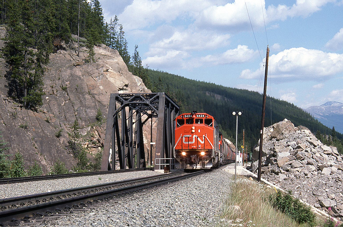 Rock faces, mountain ranges, trees and rail - Canadian railroading out west! CN SD50F 5434 and another SD lead a westbound train with a good-sized cut of colourful cylindrical hoppers on the head end, west of Jasper AB on the CN Albreda Sub. The bridges here are for the Miette River at Mile 7.8, just east of the Geikie mileboard.