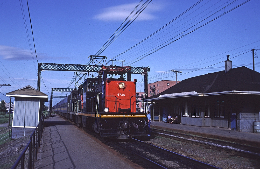 A pair of centre-cab electrics led by CN 6726 slow to a stop at Val-Royal during the evening rush hour with  a train of VIA coaches retired from intercity service.