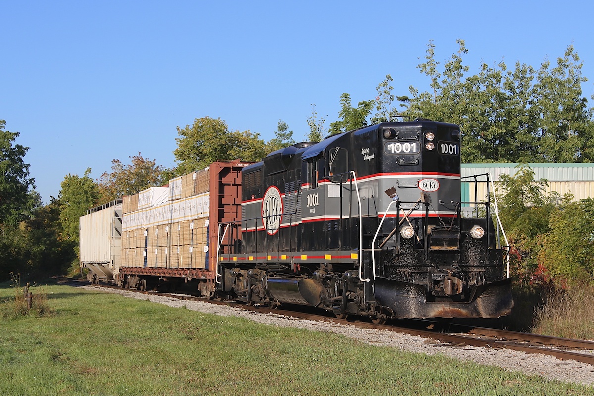 This day's BCRY train is passing through Barrie with one centre beam load of lumber for Tarpin Lumber and one hopper of sodium bentonite clay for TAG Environmental.