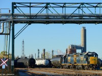 CSXT GP38-2 remote control mother 2799 is switching cars in the north end of the main Sarnia yard and is Framed in a pipeline overpass. In the background is the idle Polysar powerhouse.