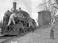 Men set about cleaning out the clogged smoke box netting. Shovels full of cinders were removed. So severe was this that the bottom of the smoke box door has a noticeable burn attesting to the high heat build-up.  Cinders plugging the frontend was said to be common characteristic of small engines such as A class 4-4-0’s and D-4 class 4-6-0’s and could be affected by too heavy a hand on the throttle of a small engine.<br><br>Engineer Charlie Waters looking back towards the camera.  Unbolting the smoke box door are:  in suit, Nels Perkins, General Locomotive Foreman, Lambton Locomotive Department and in overalls Peter Fairfull fireman on 136.<br><br>I worked for Mr.Perkins and he was fine man unlike many other officials. You didn’t get away with anything. He was the boss and everybody knew it. He just didn’t have to be a SOB.  He explained why he had this laid back manner. When he started his father was a locomotive foreman on the Algoma Division and his men all hated him. He made up his mind that when he got to be a locomotive foreman he would treat his men differently.<br><br>Peter Fairfull was a real gentleman, pleasant and easy going. He came to ourf home to ask my permission to fire 136 that trip. I agreed and the North Pool ireman who stood for the run traded off. Many men wanted this run but only 6 were needed and some would not trade off.<br><br>Peter went on to “fame” as regular engineer on the Day Transfer with 8921. I believe it was he who nicknamed that diesel Empress of Agincourt. He retired off the Havelock Budd Car. 